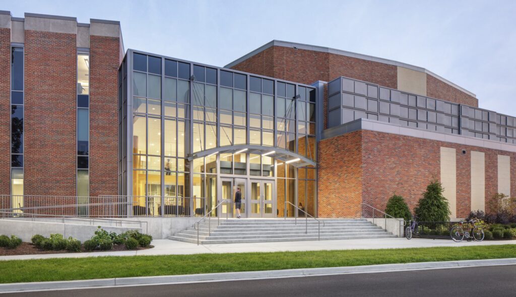 A modern building features large glass entrances and brick facades, surrounded by neat landscaping and bike racks.