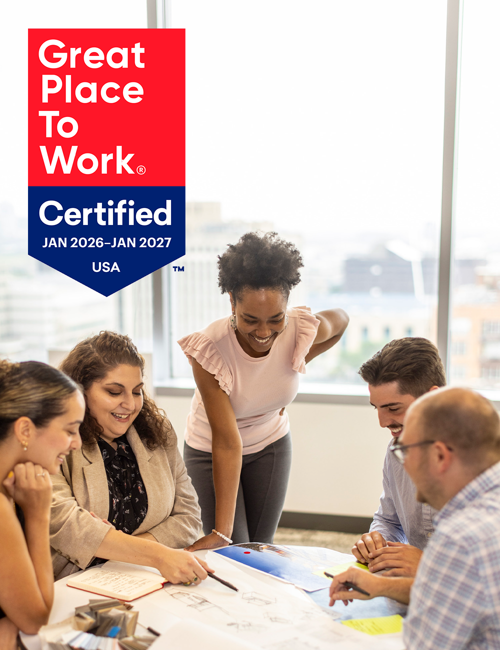 A diverse group collaborates around a table with plans, while a certification mark highlights their designation as a Great Place to Work.