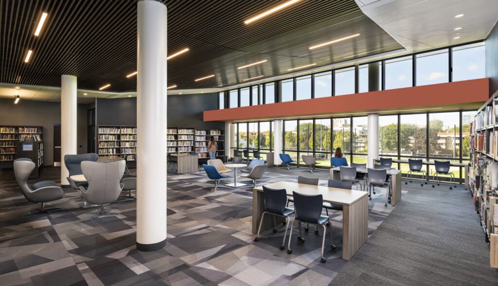 A modern high school library features large windows, comfortable seating areas, and organized bookshelves, creating a bright and welcoming study space.