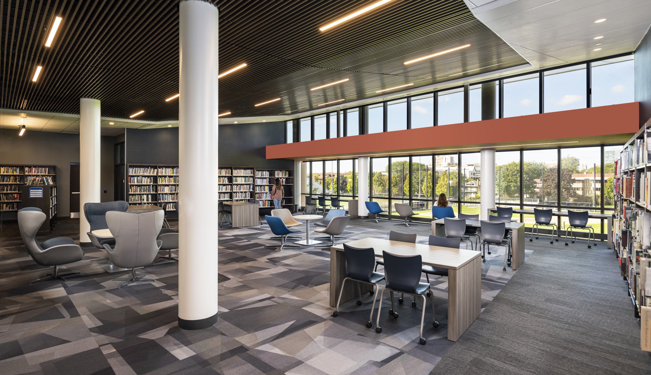 A modern high school library features large windows, comfortable seating areas, and organized bookshelves, creating a bright and welcoming study space.