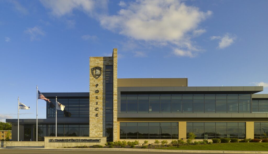 A modern fire station features a red truck in the bay, with a sleek design and green grass surrounding it, under an evening sky.