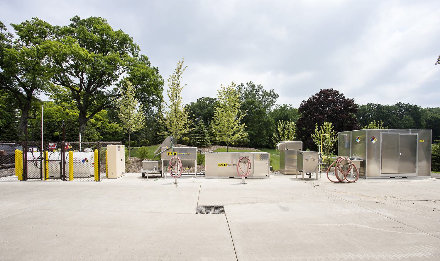A concrete area features several industrial storage units and equipment, surrounded by trees and greenery.