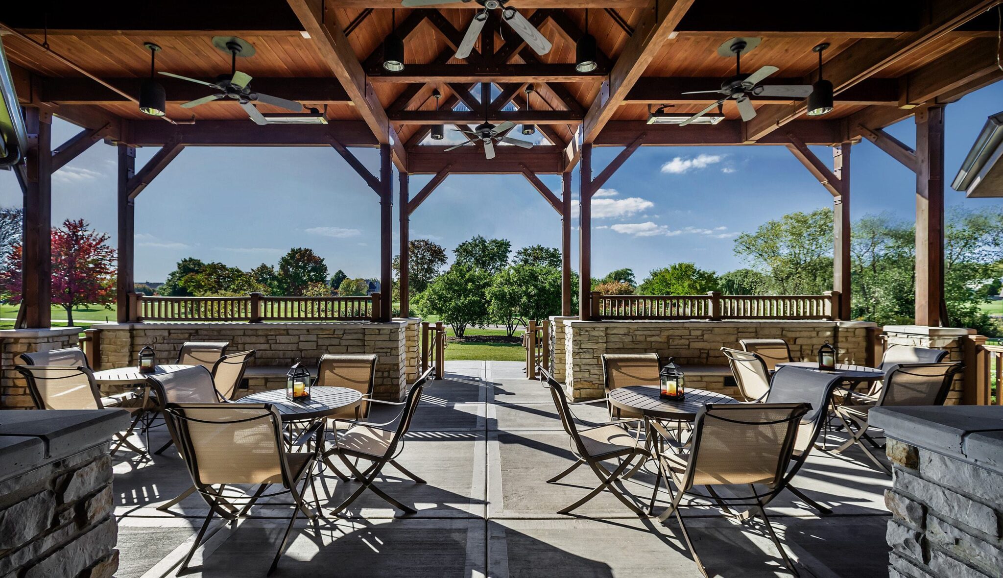 A spacious, outdoor seating area under a wooden pavilion, featuring several tables and a view of lush greenery and blue skies.