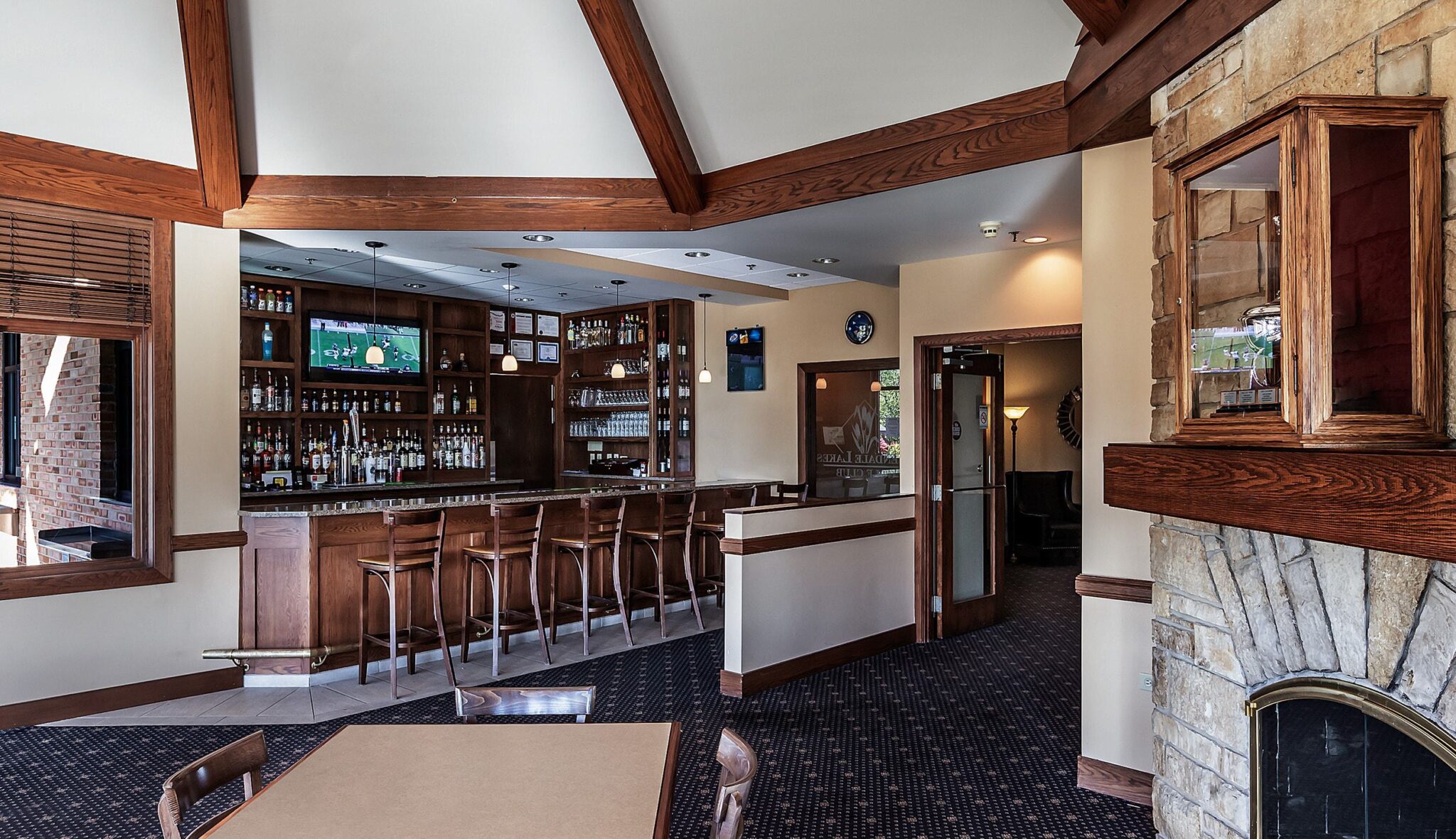 A cozy bar area features wooden beams, a stocked bar with stools, a stone fireplace, and a welcoming dining space.