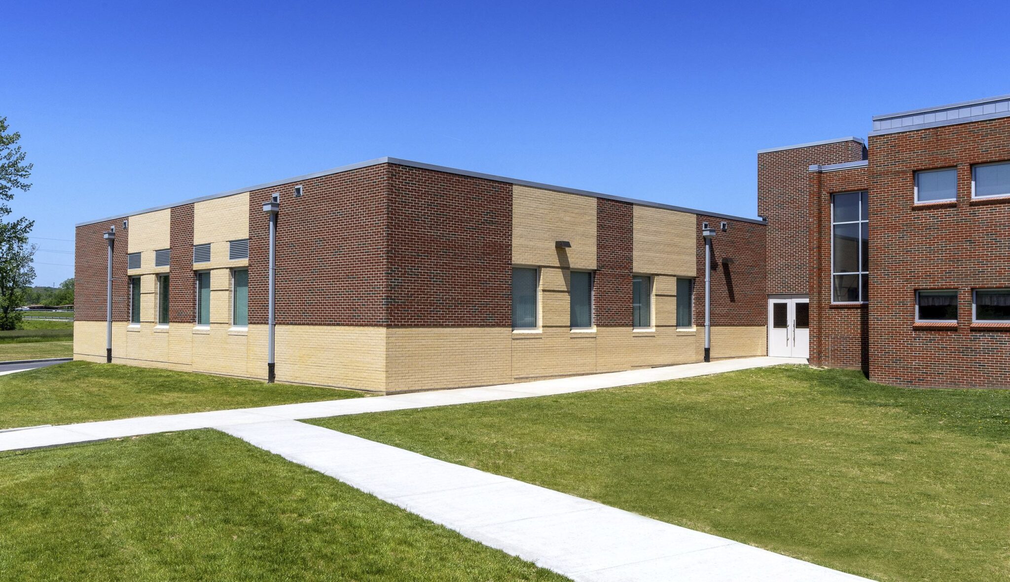A single-story brick building features a mix of light and dark tones, surrounded by green grass and a pathway under a clear blue sky.