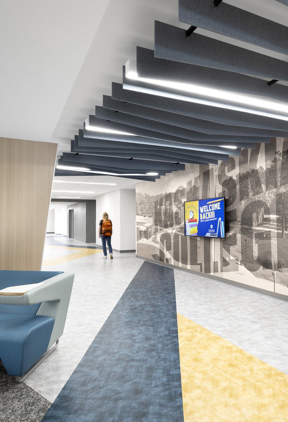 A modern hallway features unique ceiling designs, colorful flooring, and a welcoming digital display, creating an inviting atmosphere.