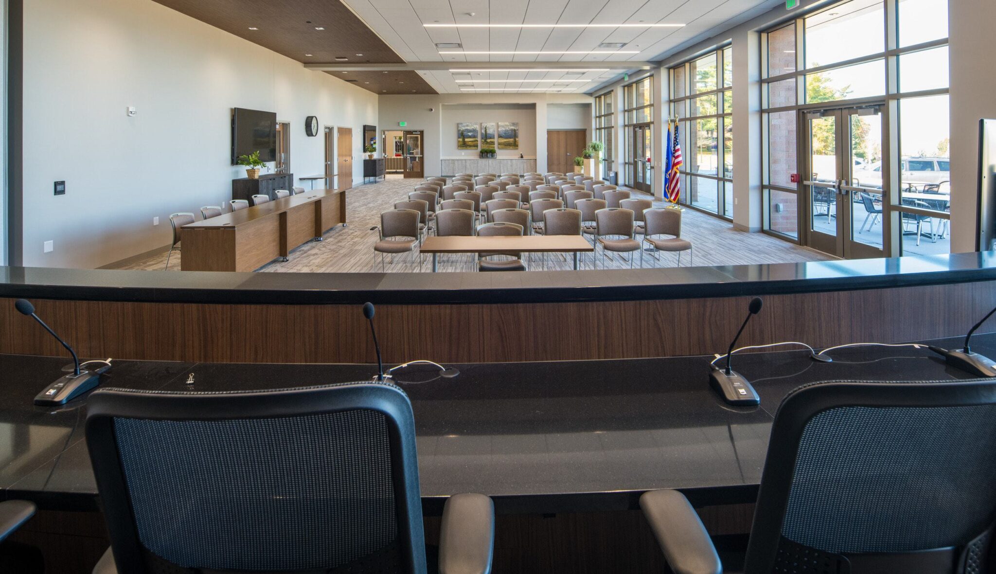A spacious meeting room features rows of chairs, a presentation area, and large windows, creating a bright, professional atmosphere.