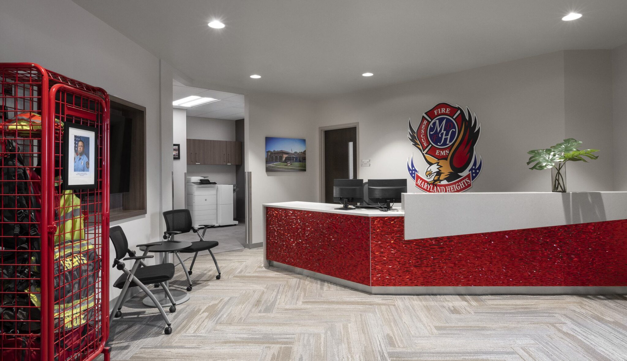 A modern reception area with a red glittery desk, seating, a framed photo, and a firefighter suit display, exuding a welcoming atmosphere.