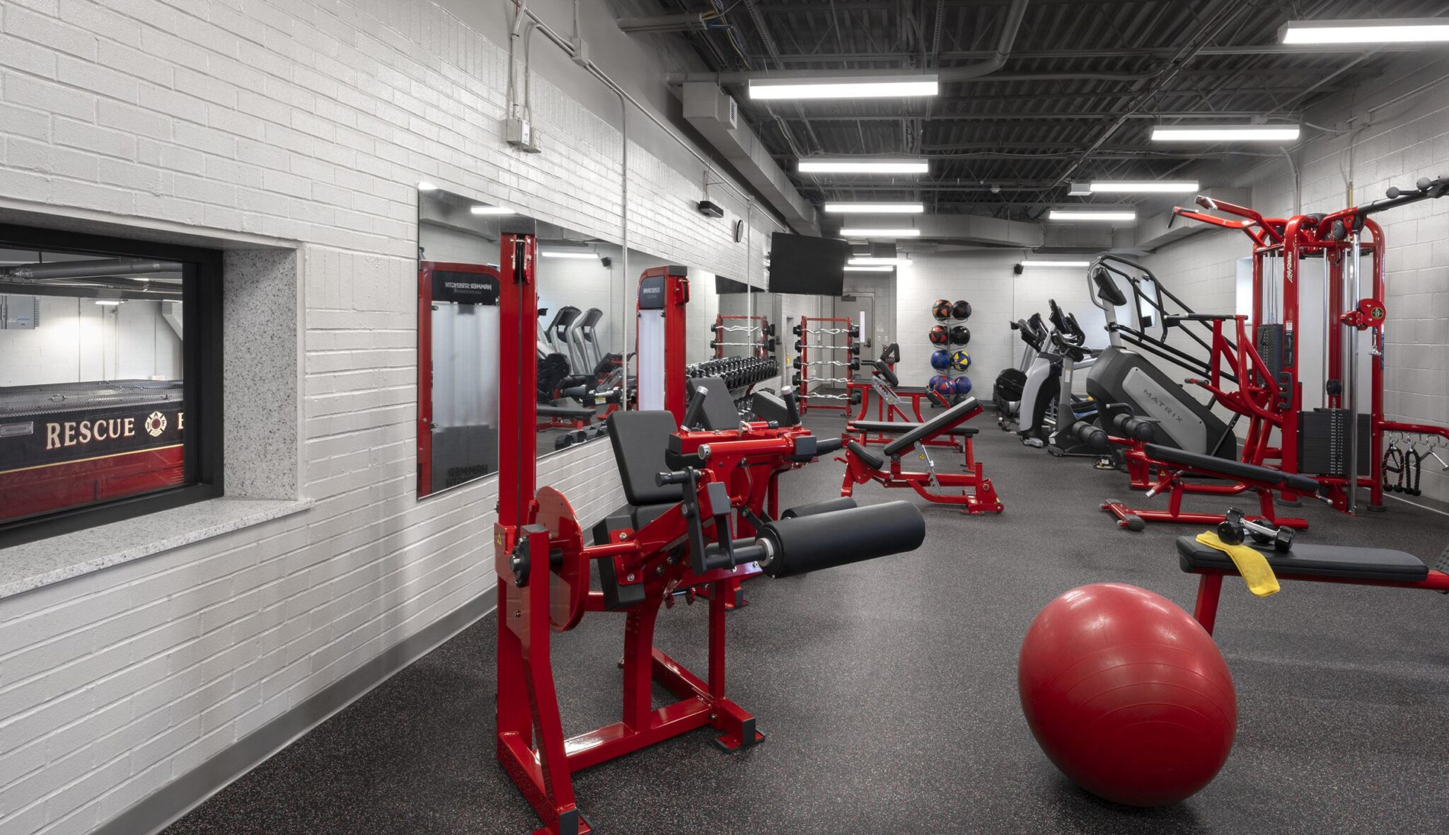 A modern gym featuring various exercise equipment, including weights and cardio machines, with a vibrant red and black color scheme.