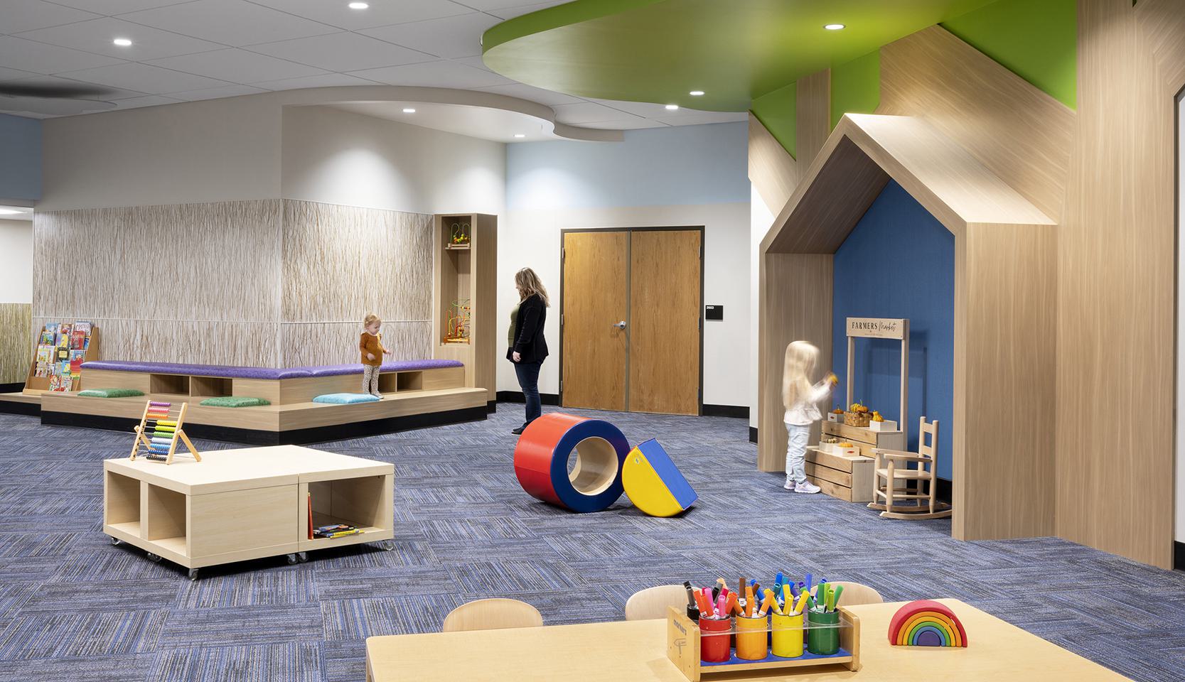 A colorful, modern playroom features various toys, a small playhouse, and children engaged in creative activities with adult supervision.
