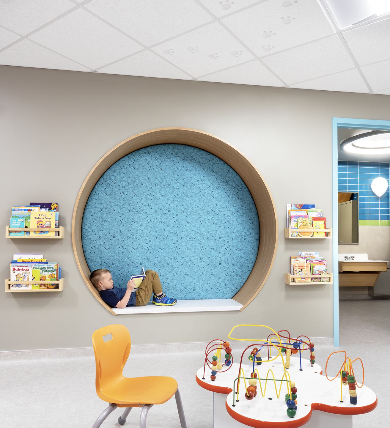 A cozy nook features a child relaxing with a book beside colorful shelves, while a play area with toys is visible nearby.