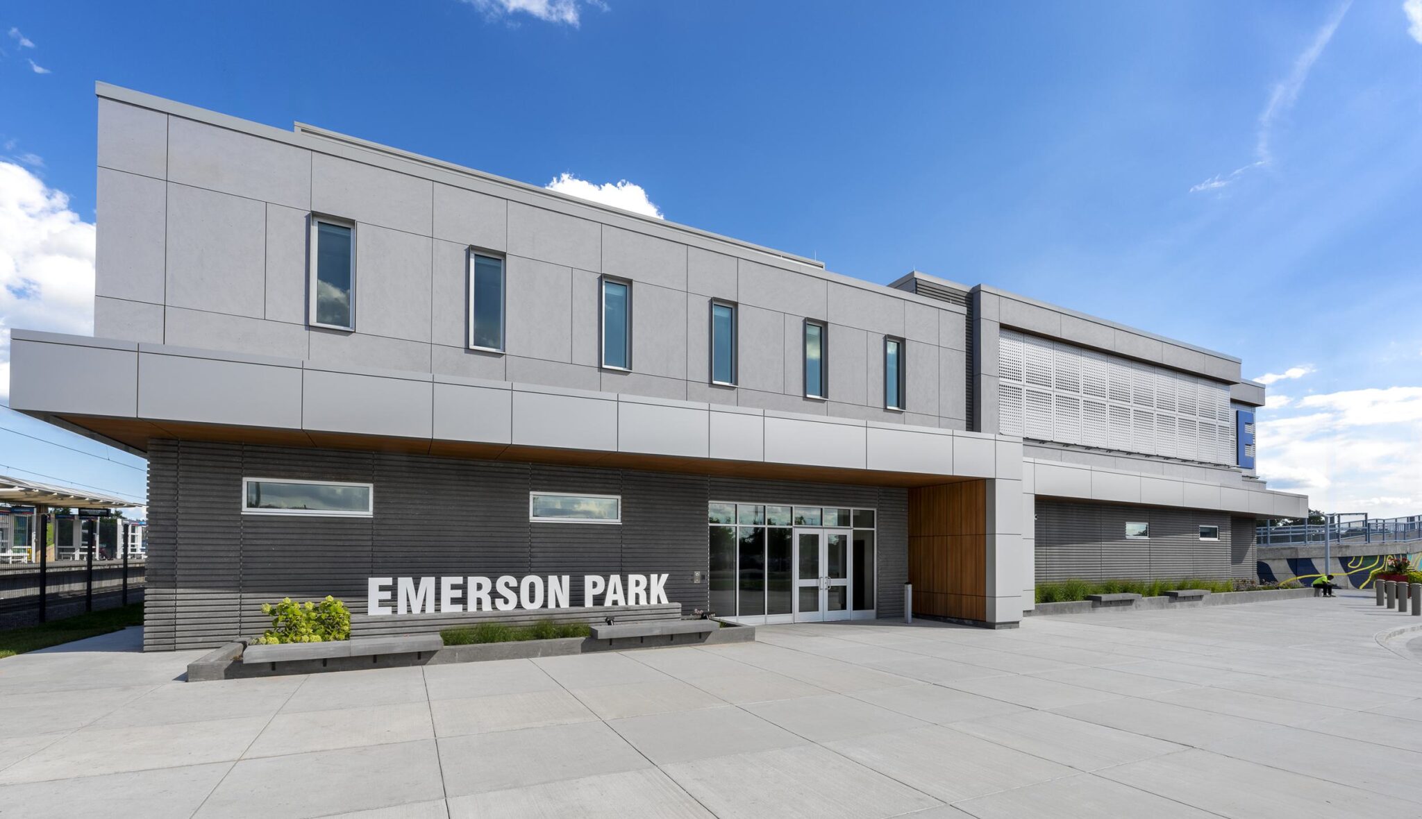 A modern building with a sleek design features large windows and a sign reading "EMERSON PARK," set against a bright blue sky.