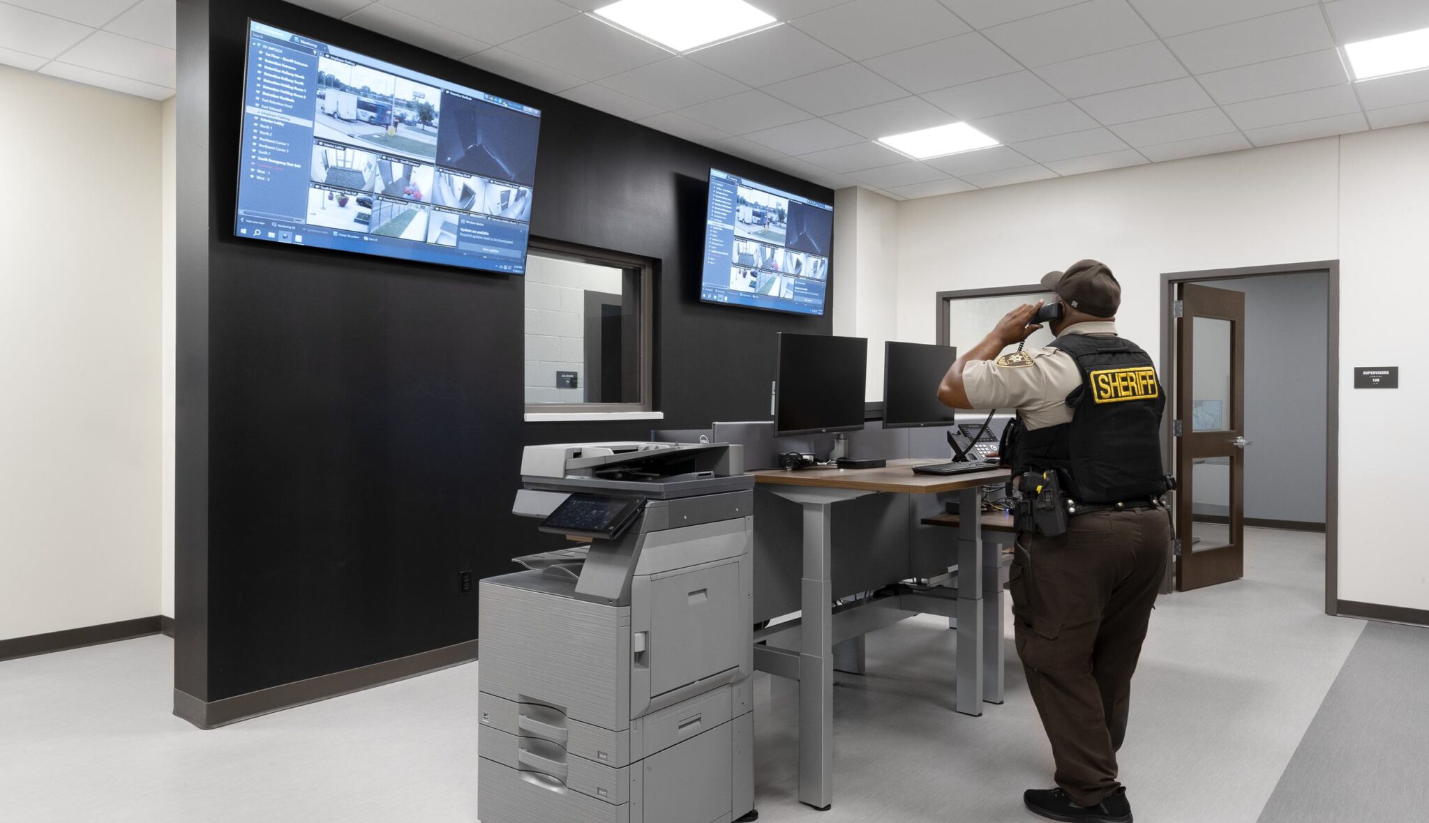 A law enforcement officer monitors security feeds in a modern control room, equipped with screens and office equipment.