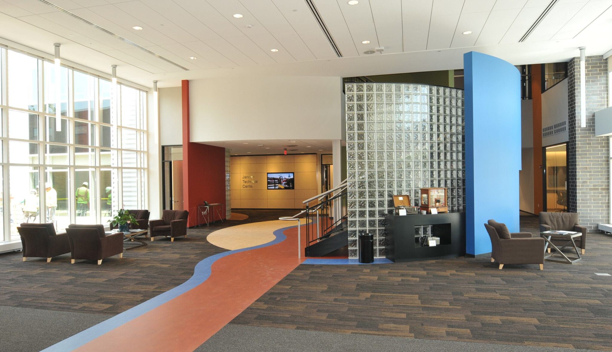 A spacious, modern lobby features colorful walls, a glass block partition, and inviting seating areas with natural light streaming in.