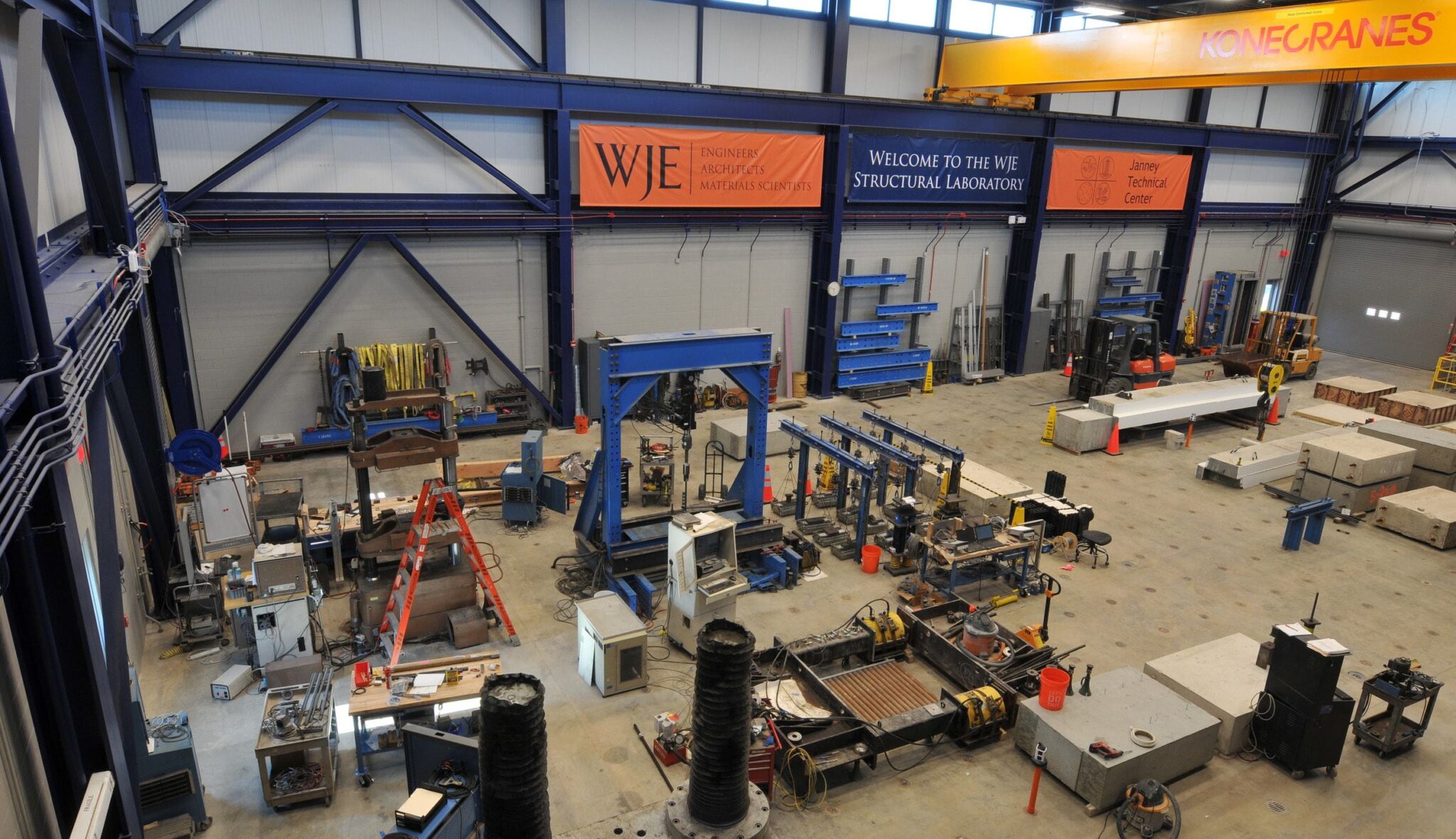 A spacious structural laboratory filled with various testing equipment, workstations, and cranes, highlighting engineering and research activities.