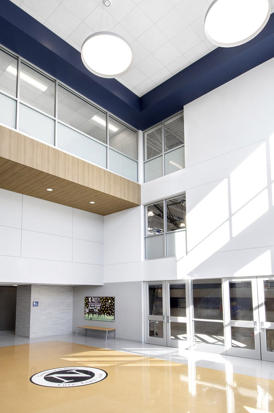 A spacious and modern athletic center features large windows, abundant natural light, and a sleek design, highlighting a central area with a logo on the floor.