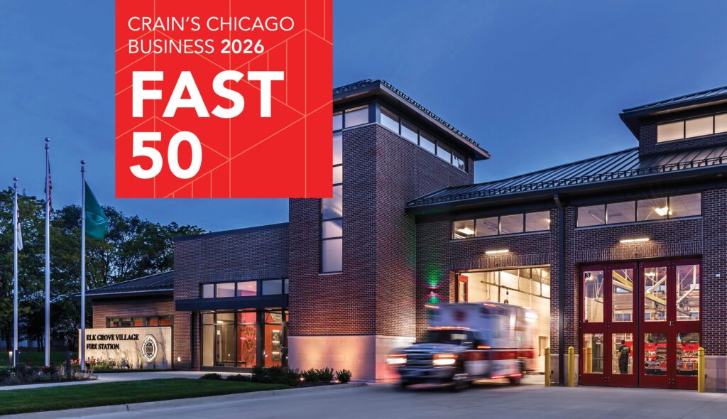A modern fire station is illuminated at dusk, featuring a red ambulance outside, with a banner announcing Crain's Chicago Business Fast 50.