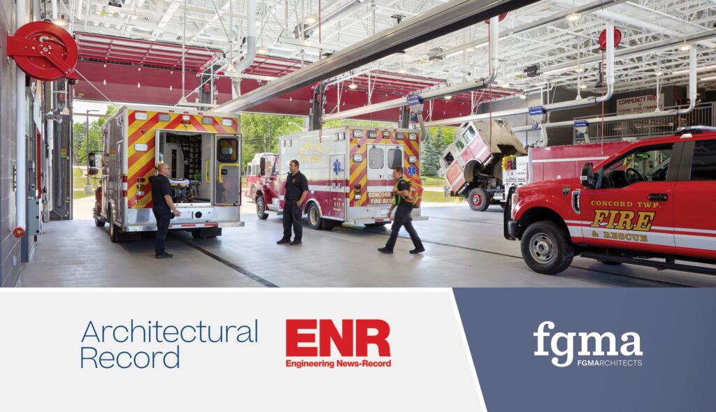 Emergency vehicles are stationed in a modern fire station, with firefighters and equipment visible in a well-lit interior space.