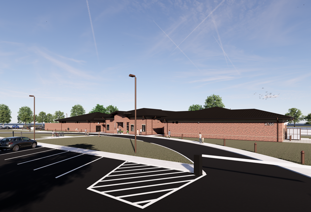 A modern brick building features a sloped roof, surrounded by green trees and a well-organized parking area with marked spaces.