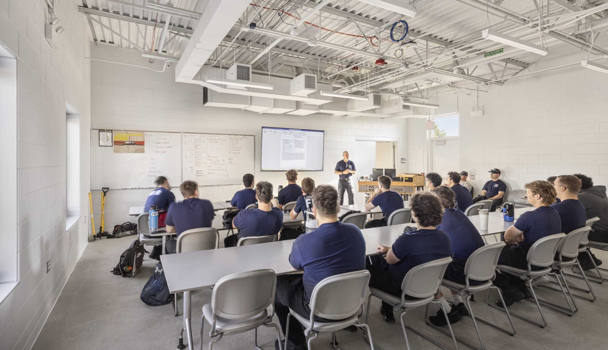 Emergency services classroom: An instructor leads a classroom training session for emergency services students at Harper College, featuring flexible tables, presentation technology, whiteboards and exposed ceiling infrastructure.