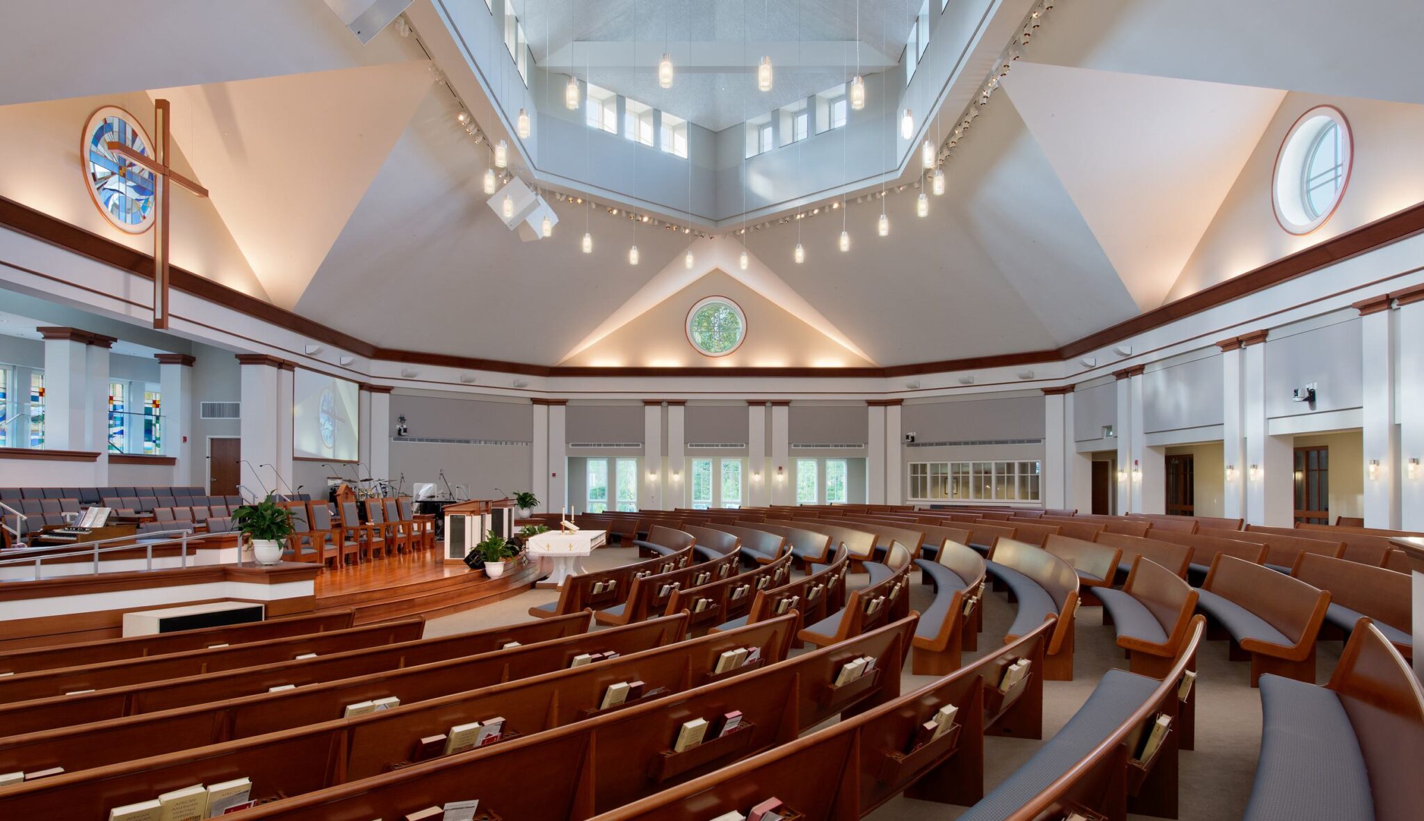 A spacious, modern church sanctuary featuring wooden pews, large windows, and a bright, geometric ceiling design.