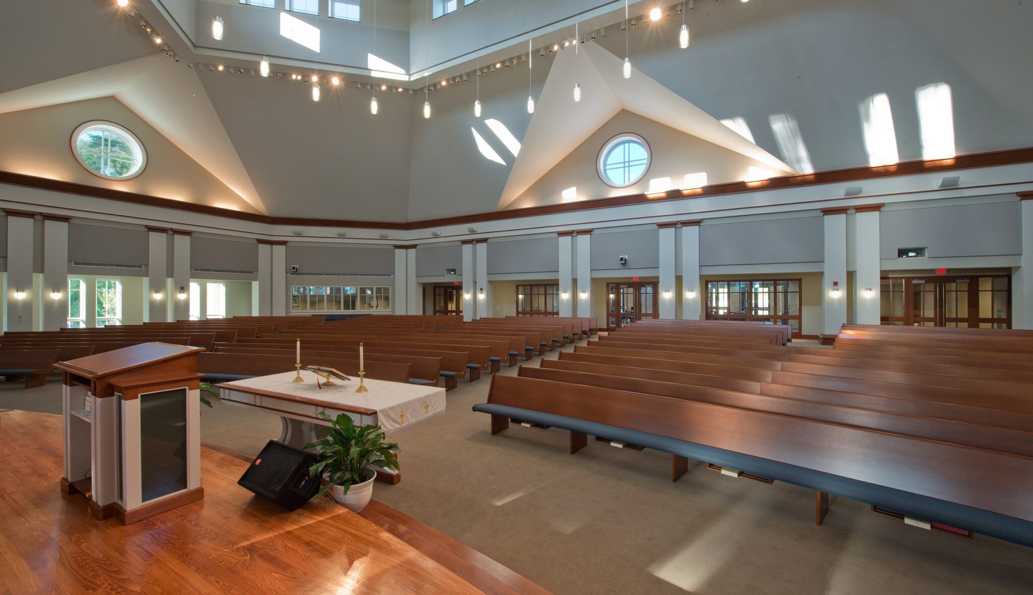 A spacious, well-lit interior of a church sanctuary, featuring wooden pews, an altar, and large windows that accentuate the architecture.