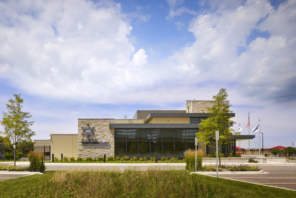 A modern building with large glass windows, featuring stone accents and greenery, set against a cloudy sky, likely serving a community function.