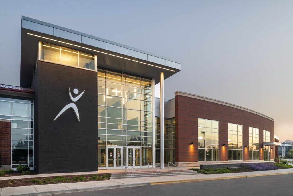 A modern building with large glass windows and a sleek design, featuring a prominent logo emphasizing wellness or fitness.