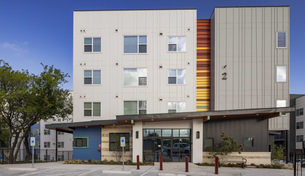 A modern multi-story apartment building features a mix of colorful and neutral facades, with a welcoming entrance and landscaped surroundings.