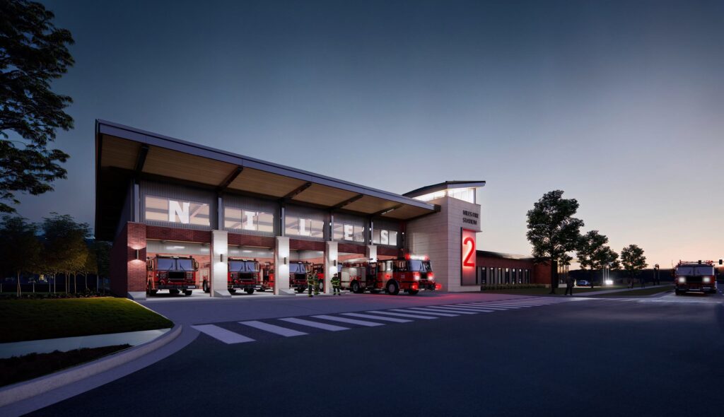 A modern fire station architectural rendering at dusk features large bays for fire trucks, illuminated signage, and a sleek design amidst a landscaped area.
