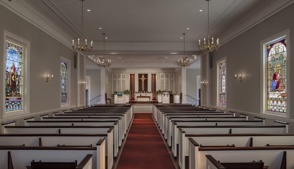 A serene interior of a church, featuring wooden pews, a central altar, and colorful stained glass windows illuminating the space.