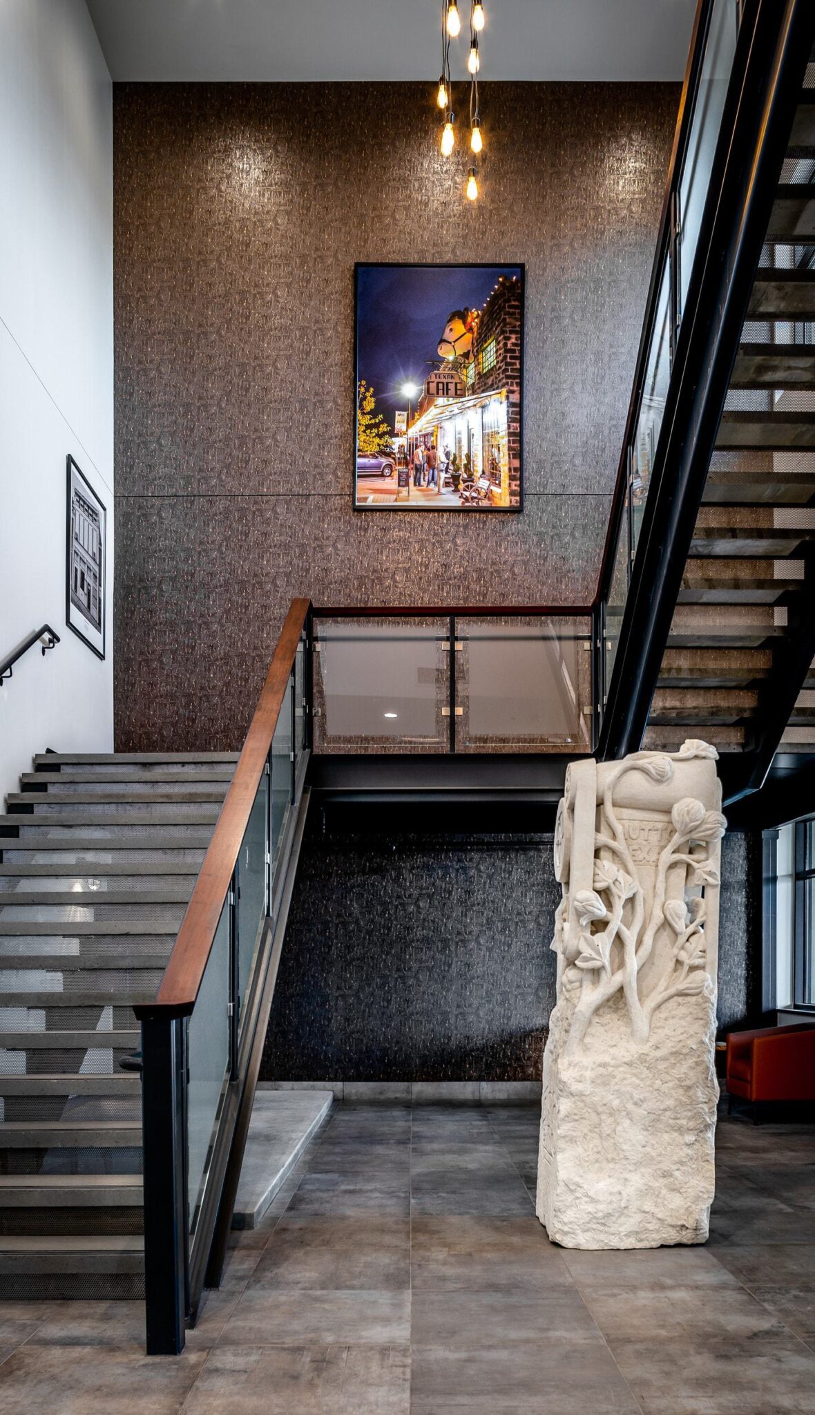 A modern staircase with glass railings leads to an upper level, featuring a decorative sculpture and a striking framed photo on the wall.