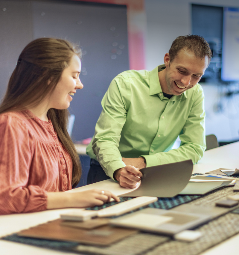 A man in a green shirt and a woman in a patterned top smile while reviewing design samples at a table.