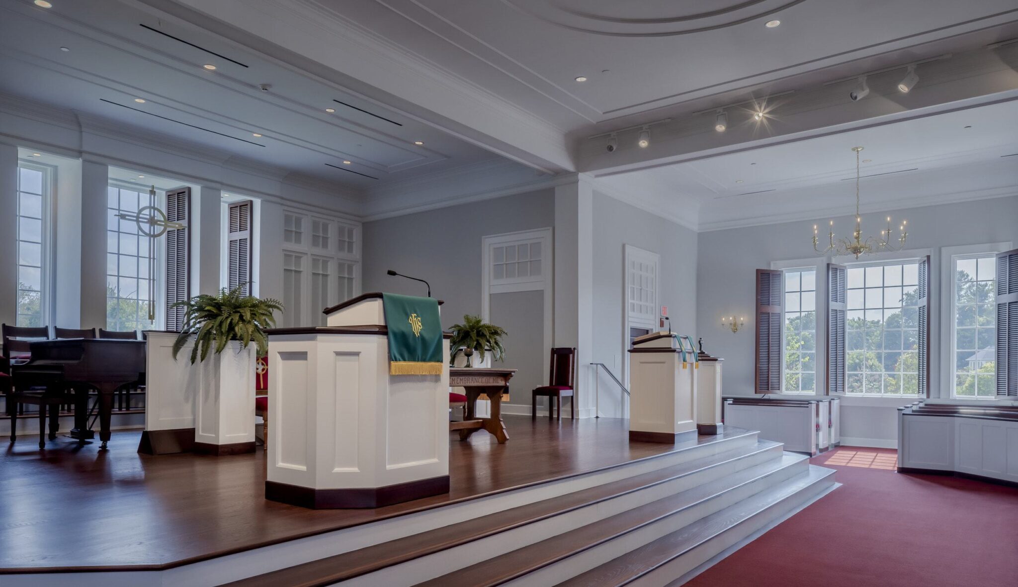 A serene, modern space features a raised platform with podiums, large windows, and elegant decor, ideal for gatherings or ceremonies.