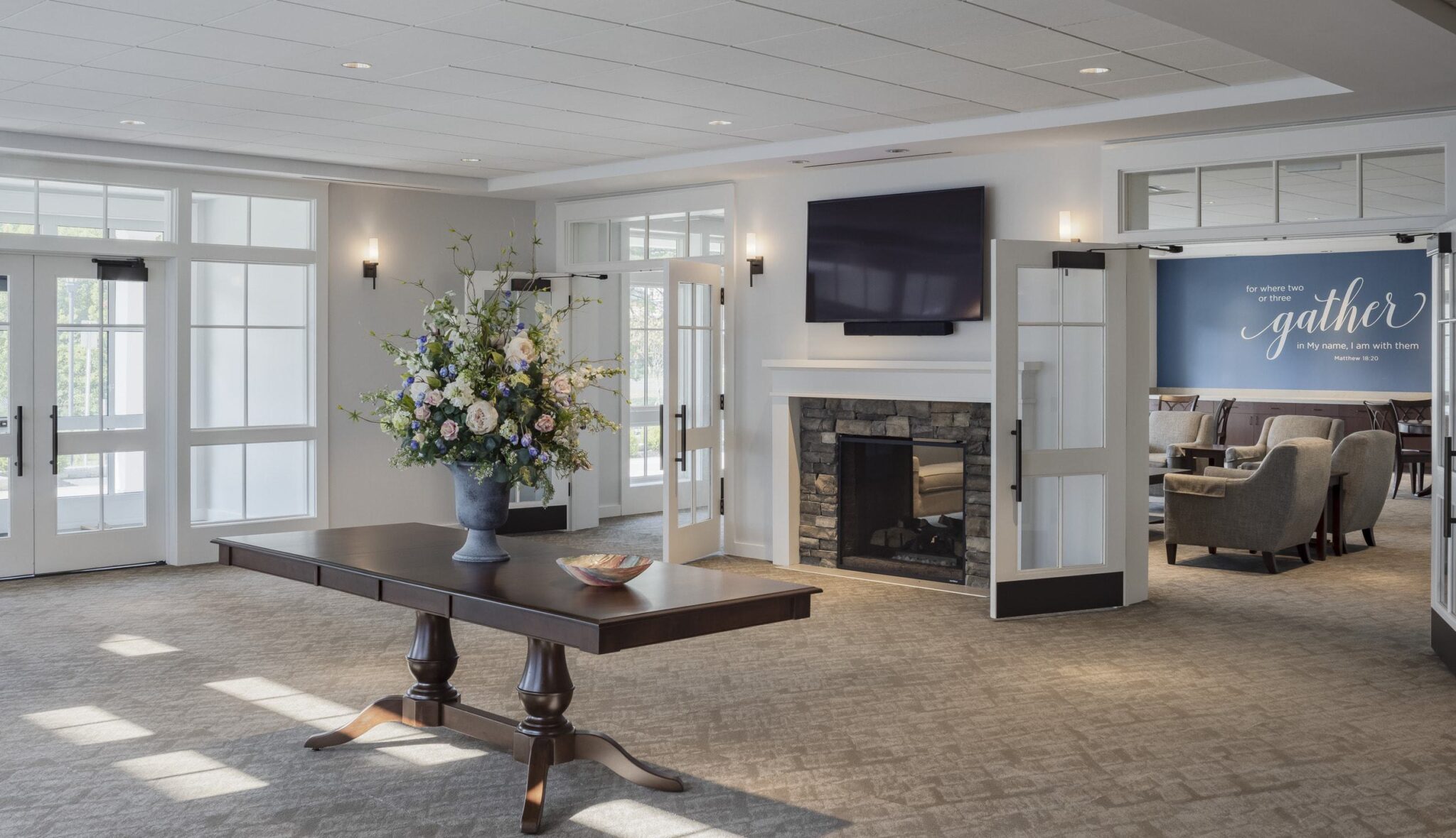 A welcoming lobby features a large table with decorative flowers, a fireplace, and seating areas, exuding warmth and comfort.