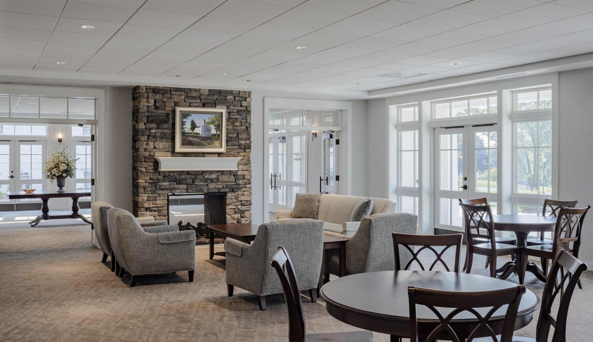 A cozy, modern lounge features comfortable seating, a stone fireplace, and large windows offering a bright and welcoming atmosphere.