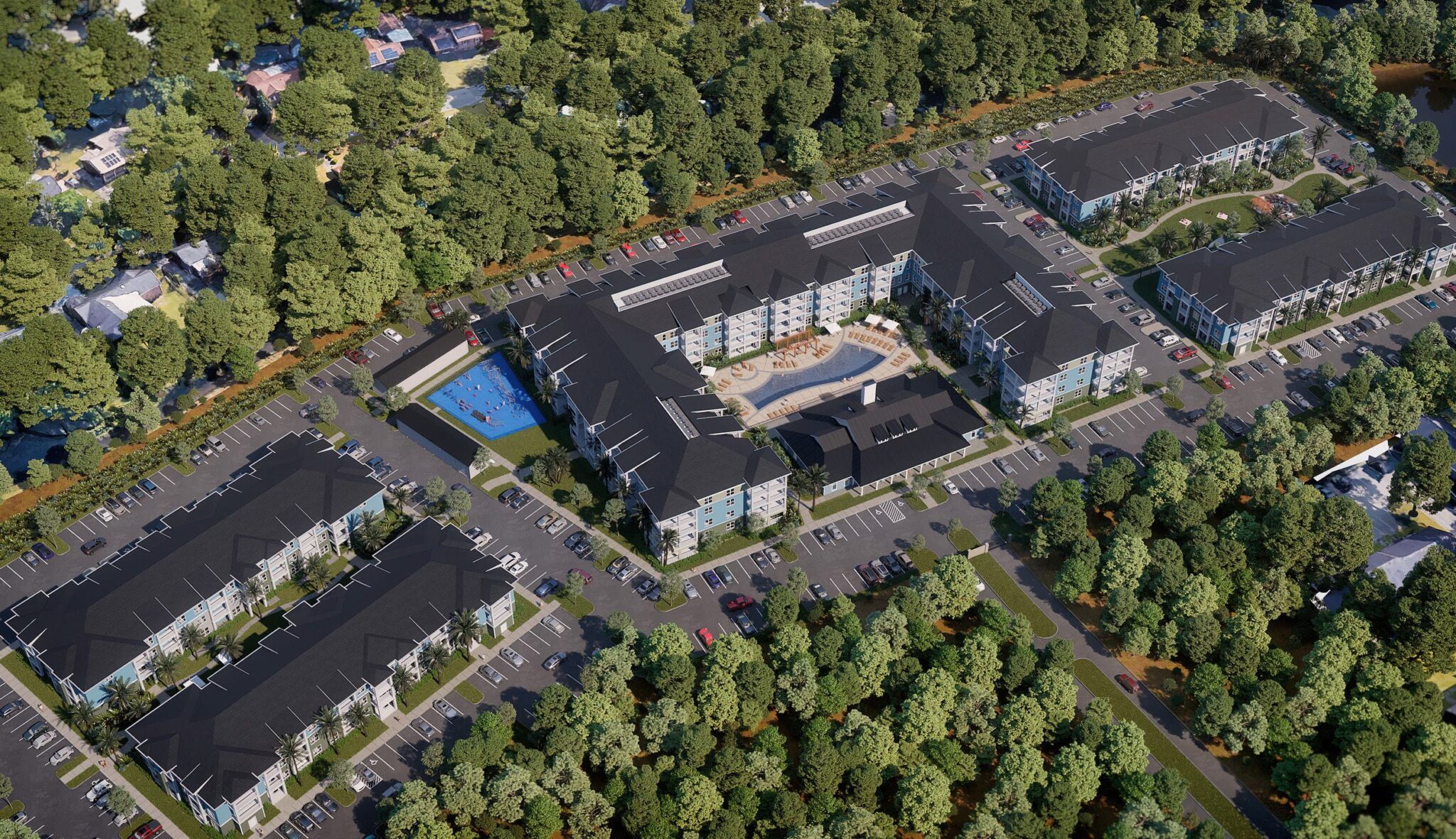 Aerial view of a modern residential complex surrounded by trees, featuring multiple buildings, a pool, and ample parking spaces.
