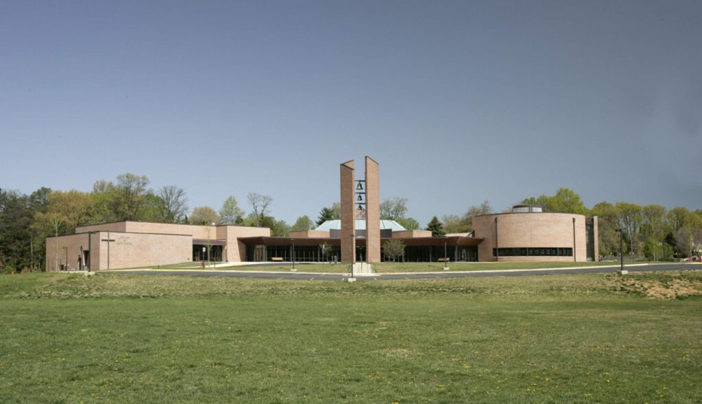 Our Lady of Good Counsel Catholic Church with brick exterior, large windows, set on a grassy area, surrounded by trees.