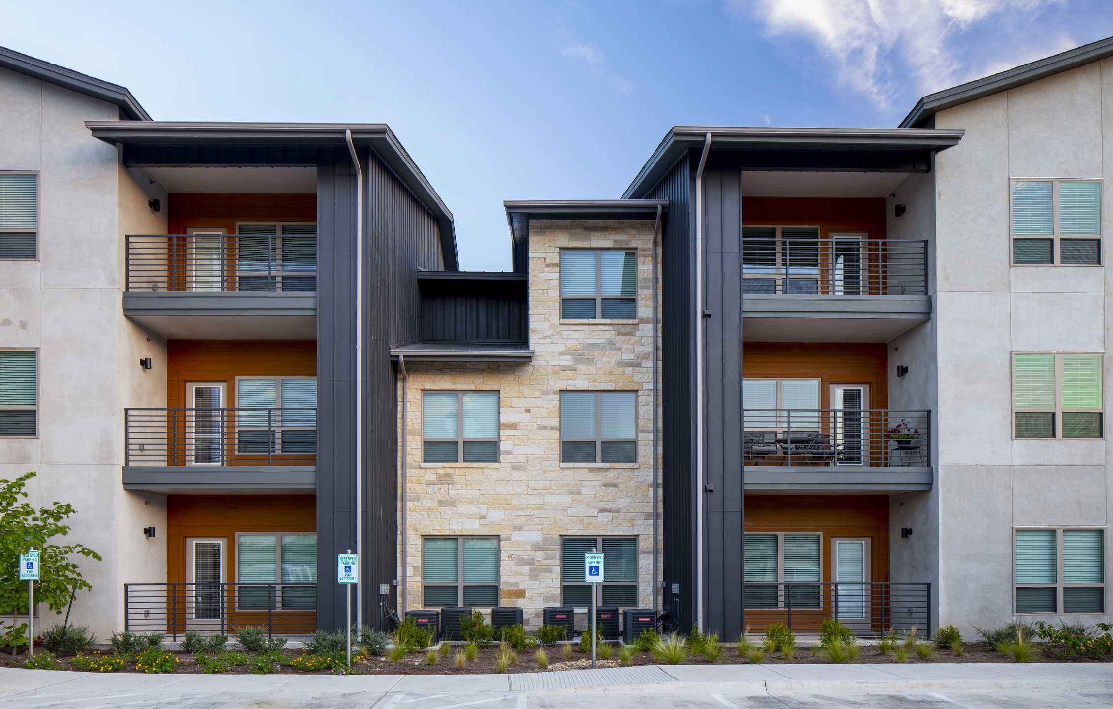 Modern multilevel apartments featuring a mix of stone and sleek metal exteriors, with balconies and landscaped surroundings.