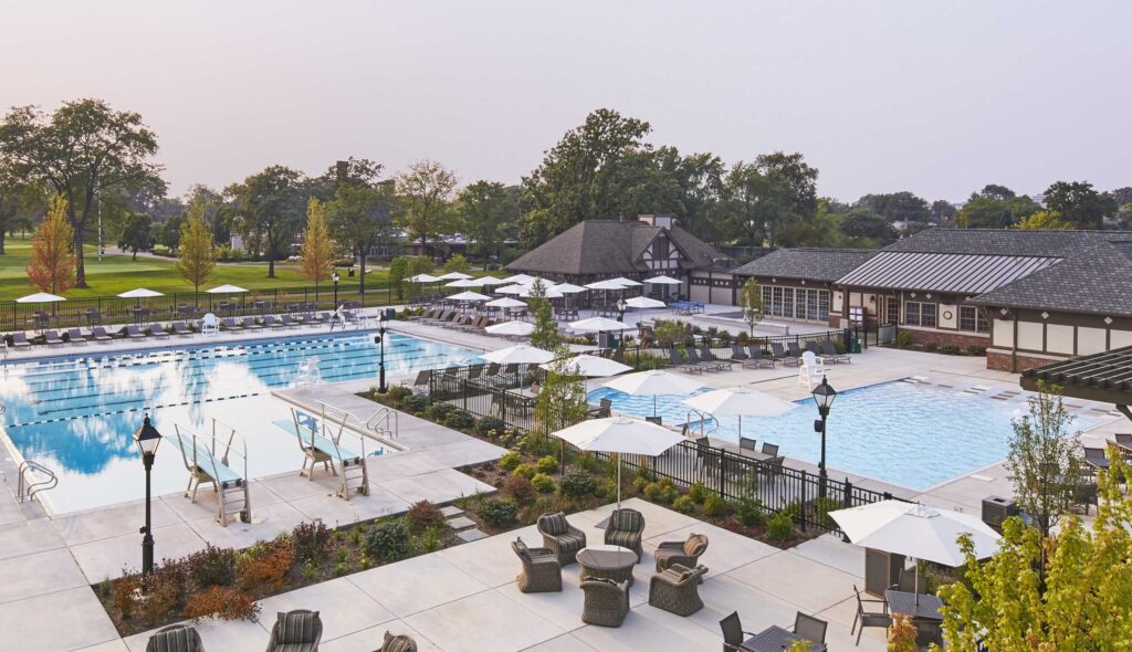 A serene outdoor area features two pools surrounded by lounge chairs, umbrellas, and well-maintained landscaping, offering a relaxing atmosphere.
