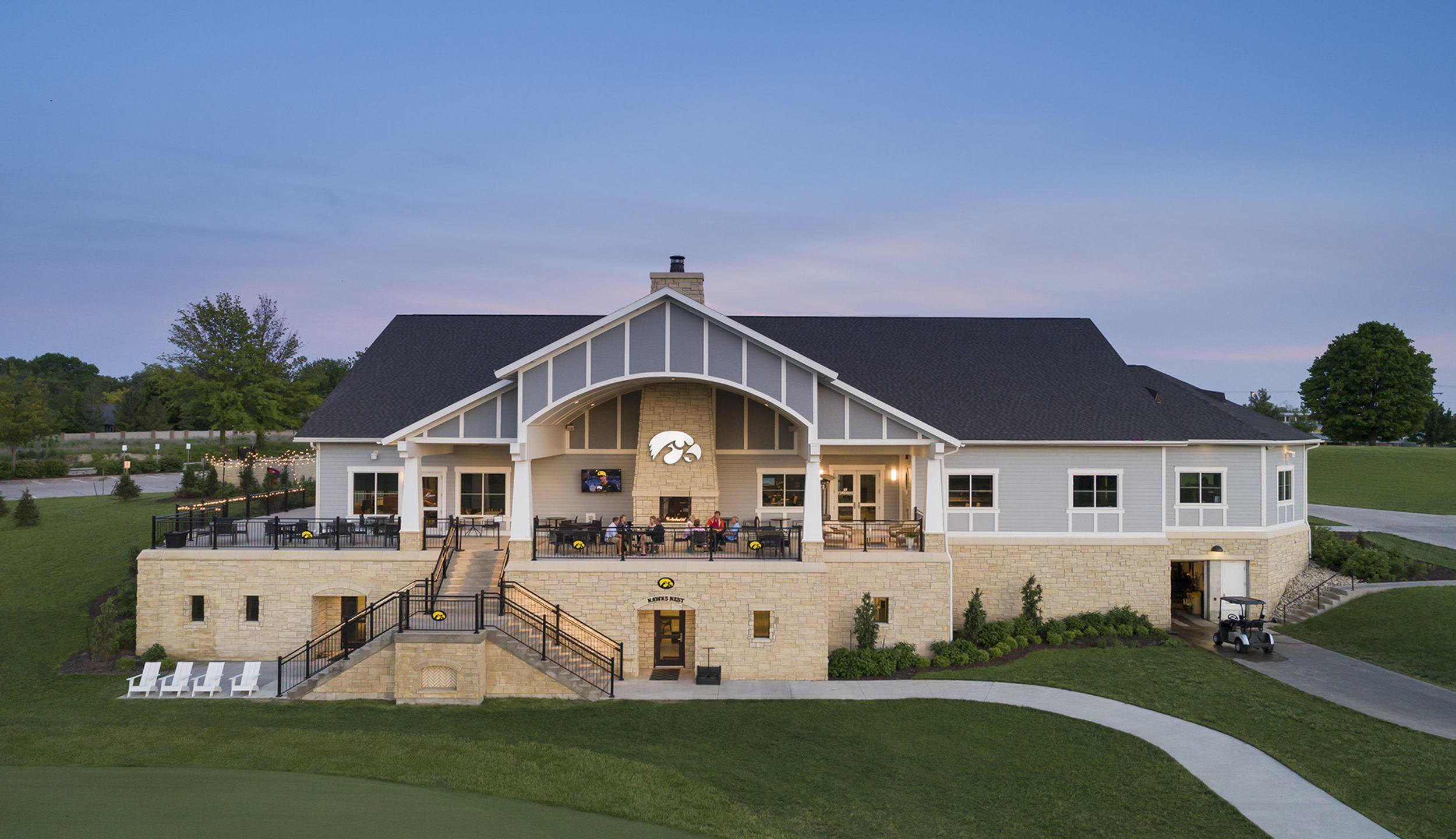 A modern clubhouse features a spacious patio and elegant architecture, set against a serene landscape at dusk.