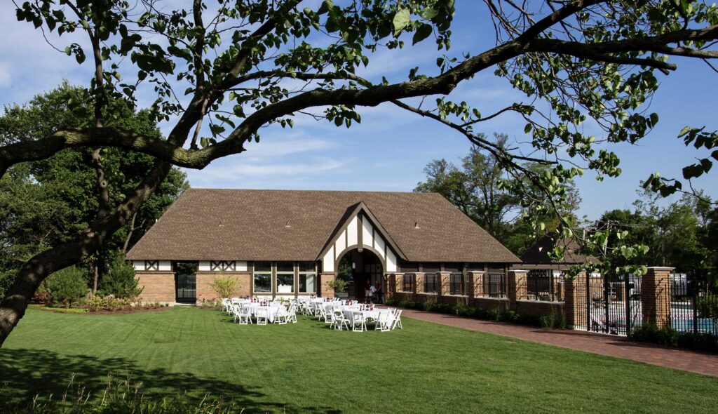 A charming building with a sloped roof, surrounded by greenery, hosts a row of white chairs set up for an outdoor event.