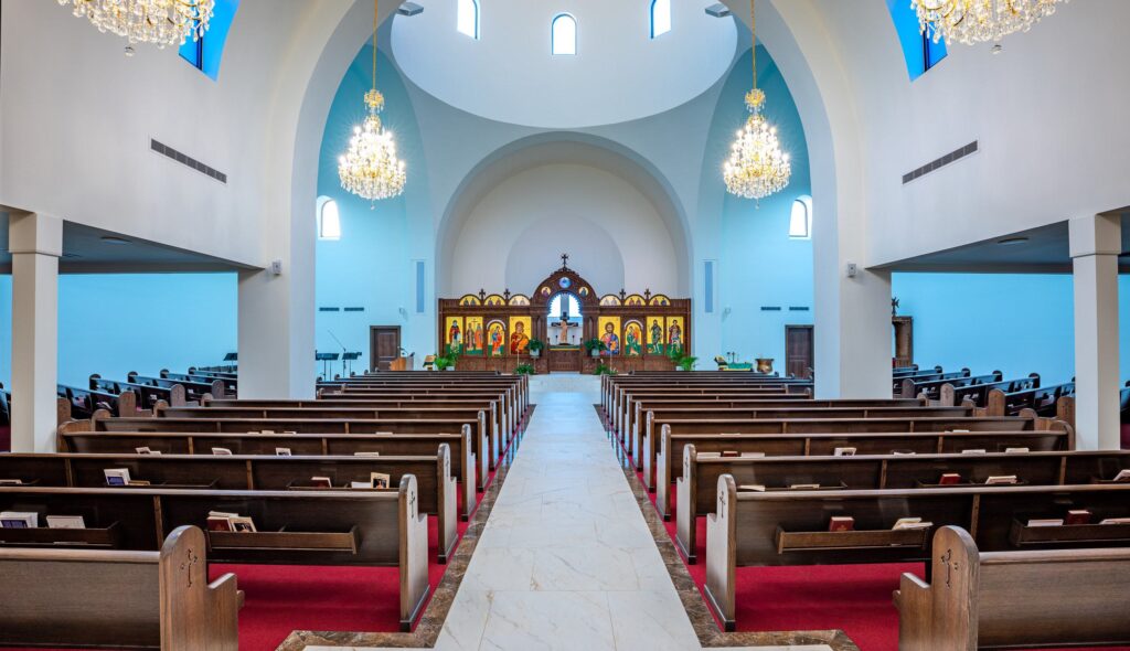 A spacious church interior featuring pews, ornate chandeliers, and an altar adorned with religious icons, bathed in soft blue light.