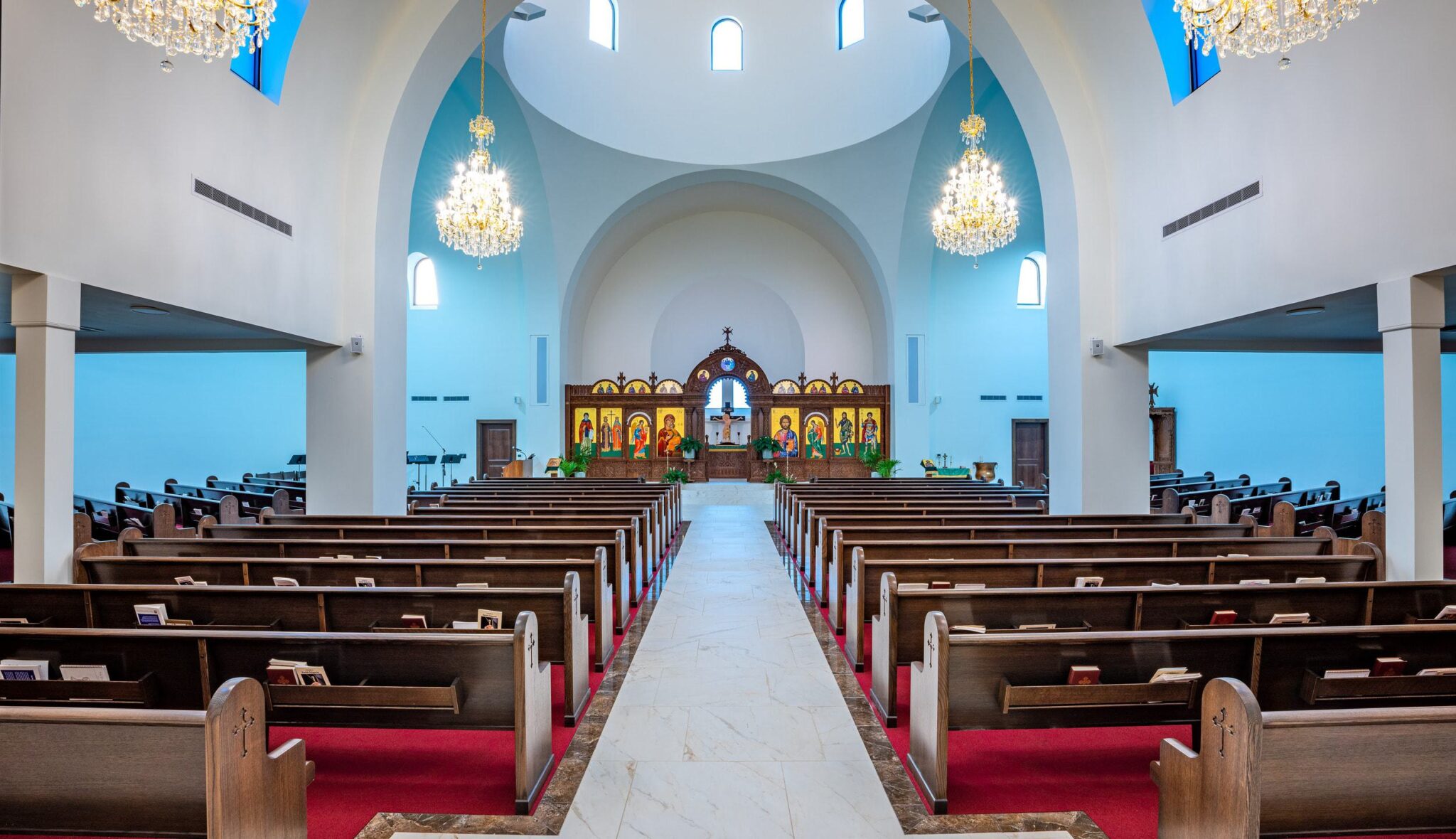 A spacious church interior featuring pews, ornate chandeliers, and an altar adorned with religious icons, bathed in soft blue light.