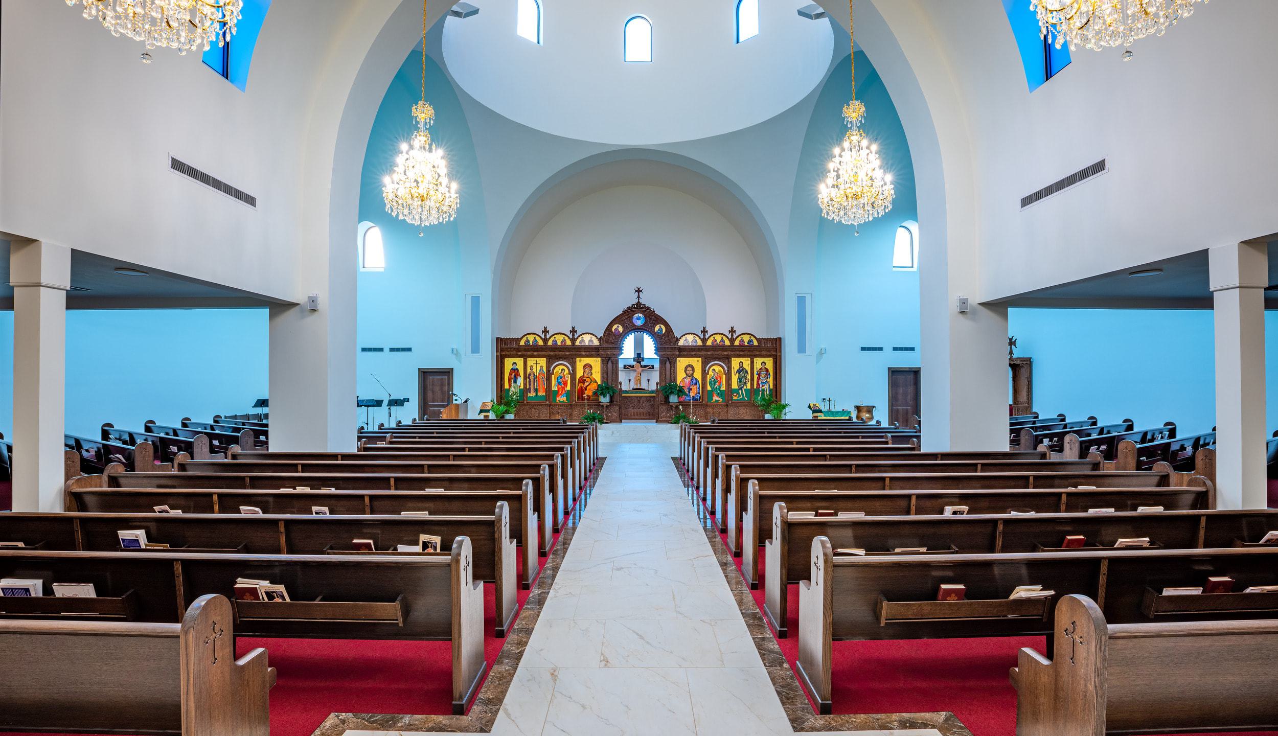 A spacious church interior featuring pews, ornate chandeliers, and an altar adorned with religious icons, bathed in soft blue light.