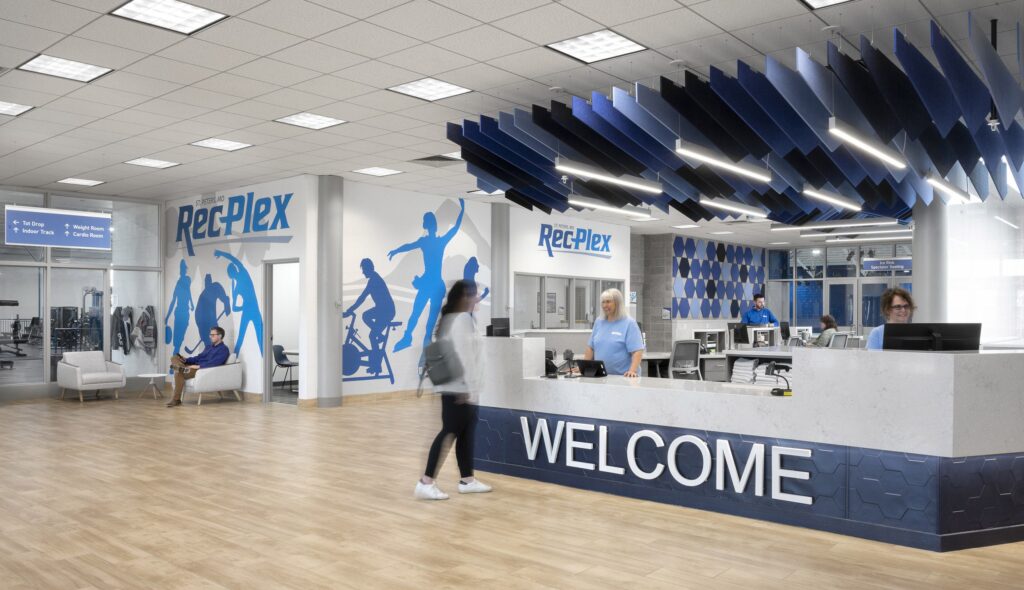 A modern fitness center reception area features a welcoming desk, fitness-themed decorations, and patrons engaging in various activities.