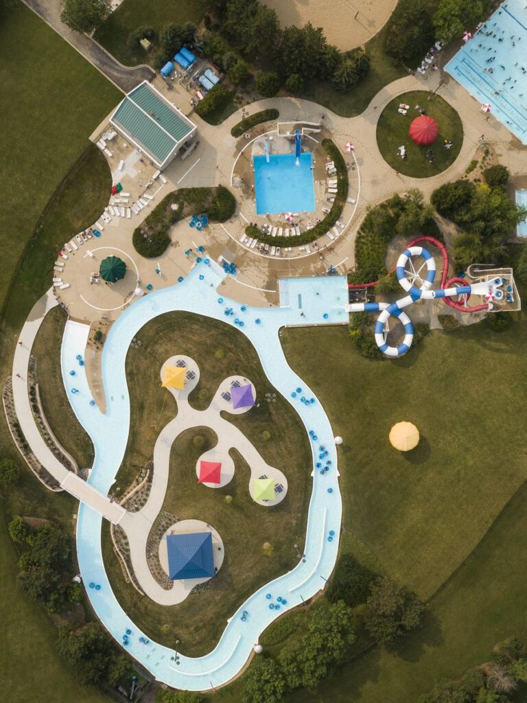 An aerial view of a water park featuring a lazy river, pools, colorful slides, and lush greenery surrounding the recreational area.