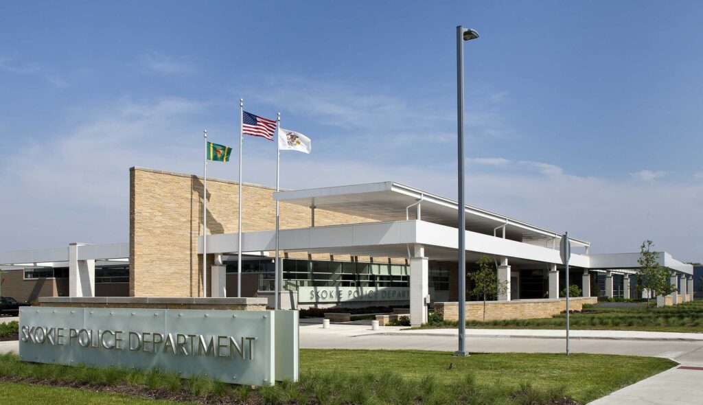 Skokie Police Department, a modern adaptive reuse building featuring contemporary architecture, large windows, and flags displayed outside in a landscaped area.