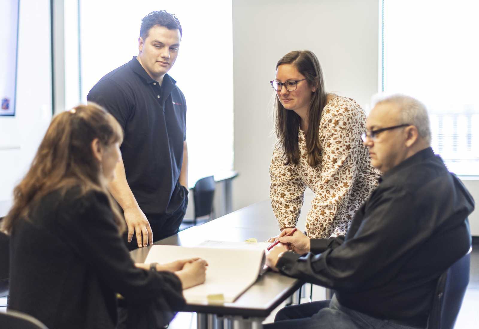 A group discusses around a table, with four individuals engaged in conversation, sharing ideas and collaborating on a project.