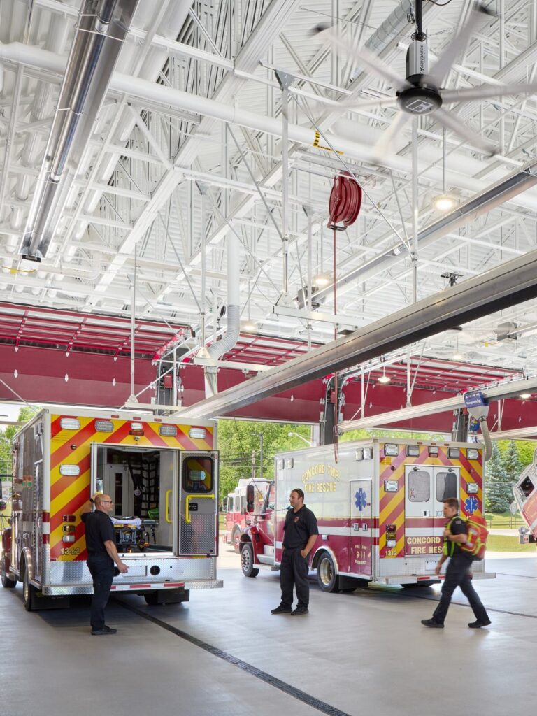 Emergency responders work in a modern fire station, preparing equipment and vehicles in a bright, spacious garage.